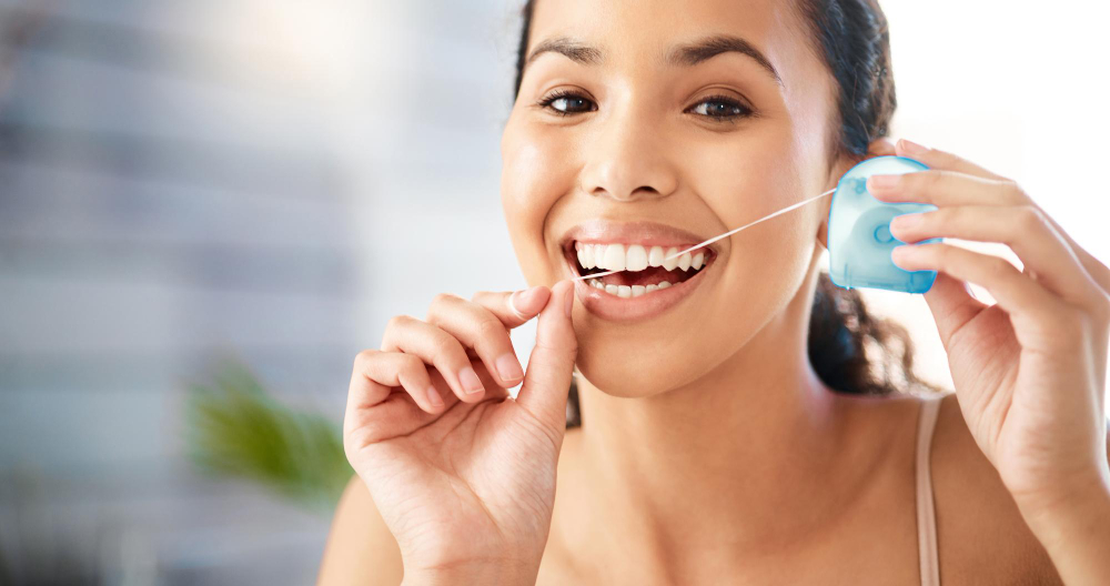 Prevenção de doenças gengivais: mulher cuidando dos dentes, passando fio dental.