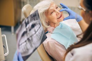 Mulher sorridente olhando para o espelho após tratamento odontológico, representando o atendimento humanizado e eficaz oferecido pela Uniodonto Cooperativa Odontológica.