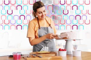Microempreendedora confeiteira sorridente, de avental cinza, cobrindo um bolo rosa na cozinha; imagem usada para ilustrar os benefícios de um plano odontológico para MEI.